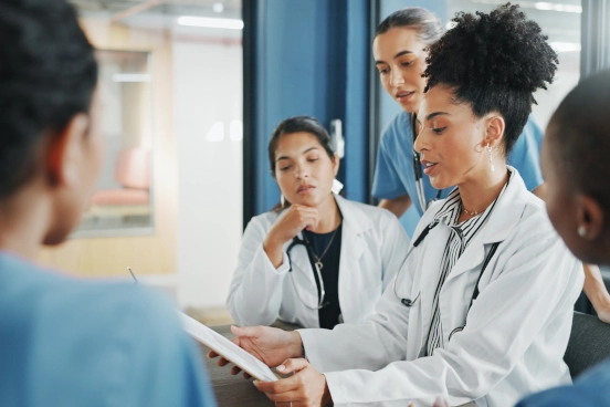 A photograph of several medical professionals discussing the content of a tablet device.