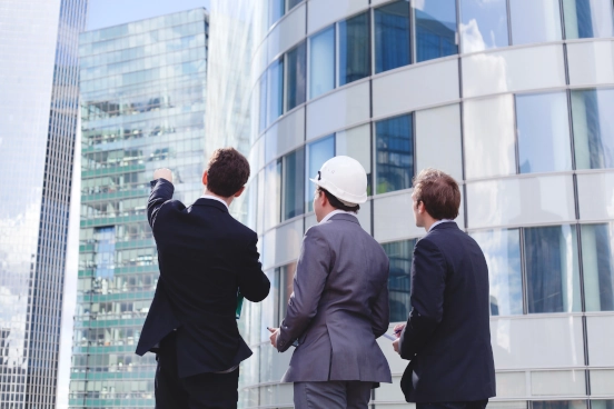 An image of three people in front of a building pointing towards it. One of the people are wearing a hard hat.