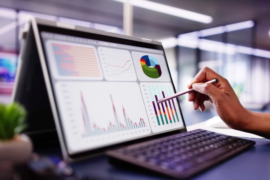 A laptop screen showing multi coloured graphs with a person holding a stylus against the screen