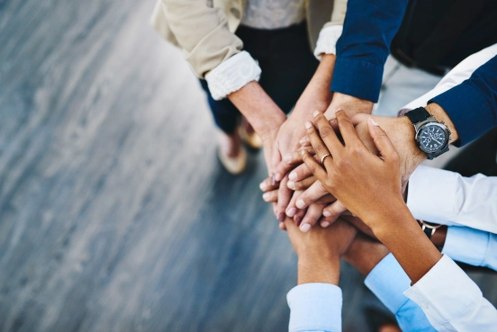 A close-up photograph of 10 hands lying over the top of each other signifying inclusion