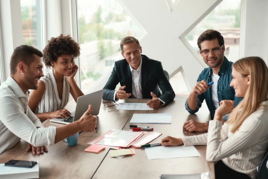 An image showing five people gathered around a desk in an office in discussion.